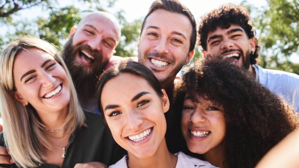 A group of people (three men and three women) taking a photo on a sunny day in a park. Everyone is smiling.
